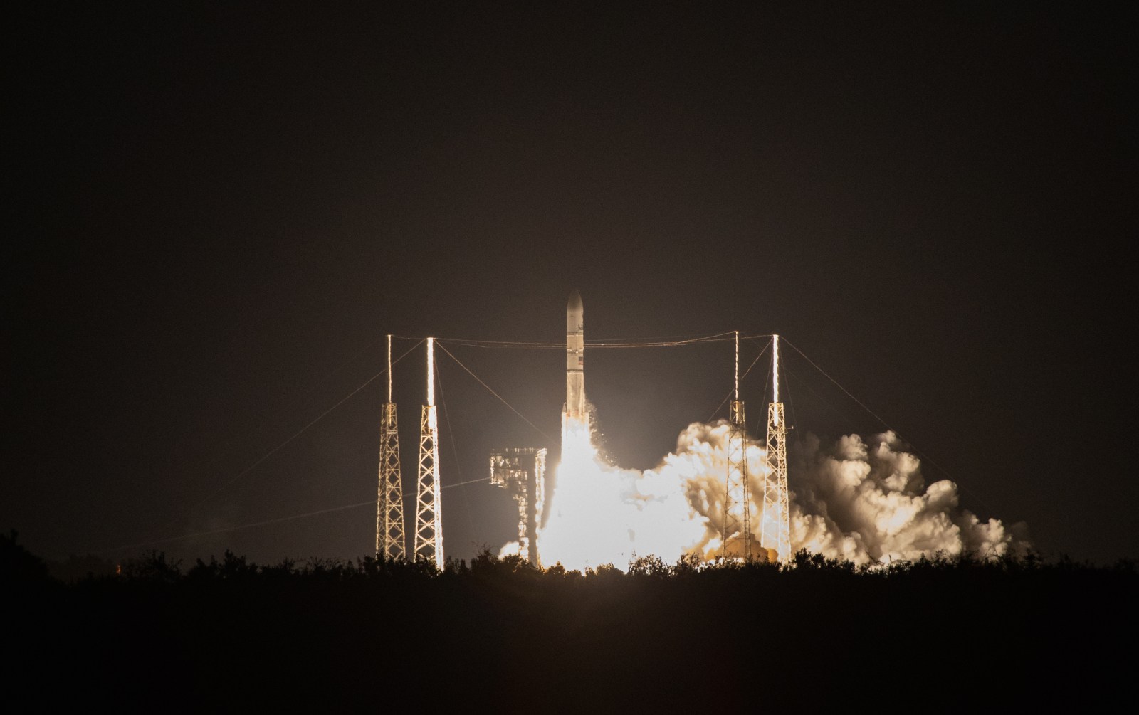 A Vulcan rocket lifts off between the lightning towers of Space Launch Complex 41 in a night launch.