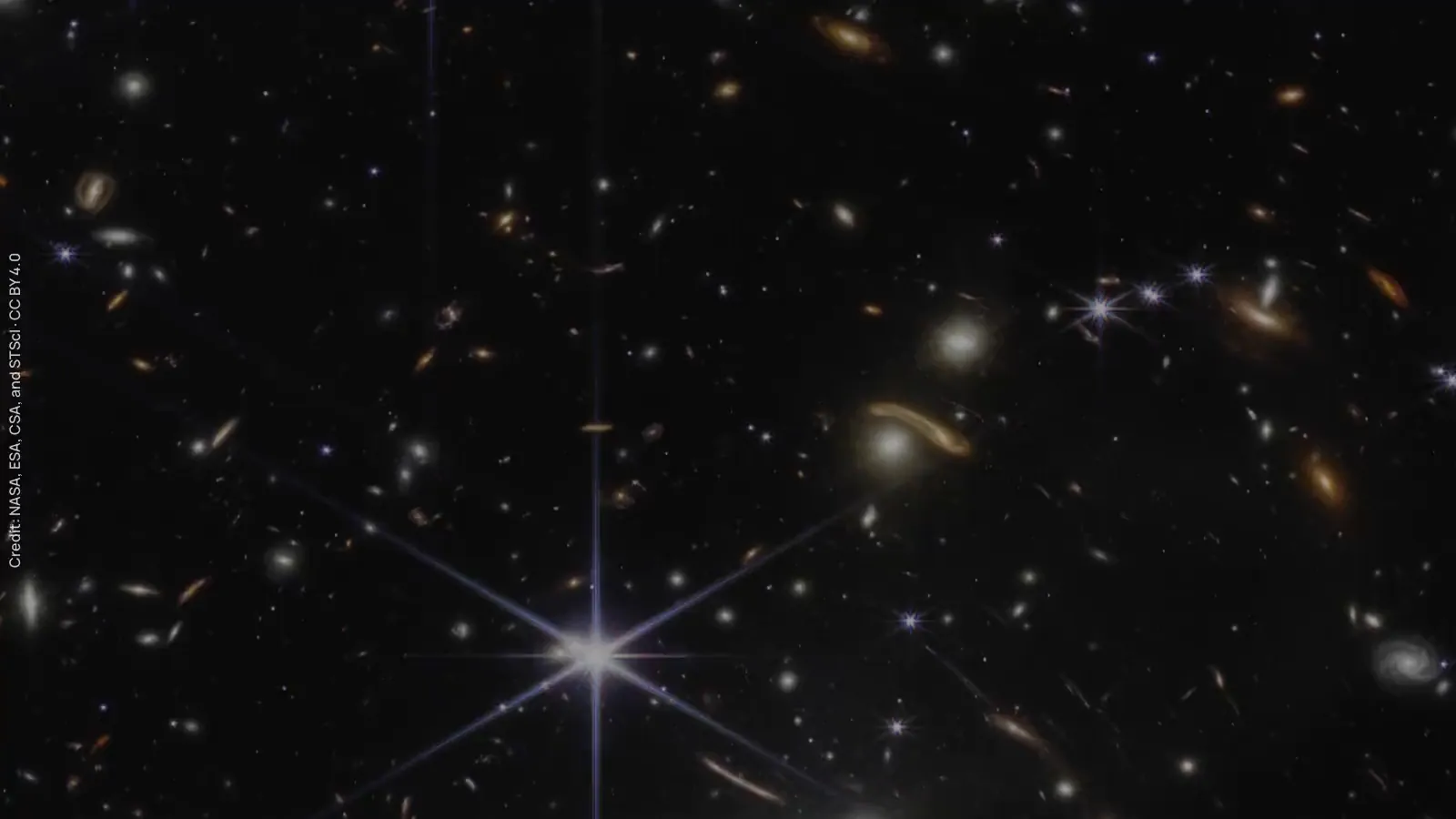 Video: a slow drift across thousands of galaxies, some stretched into glowing arcs, around a bright six-pointed star.