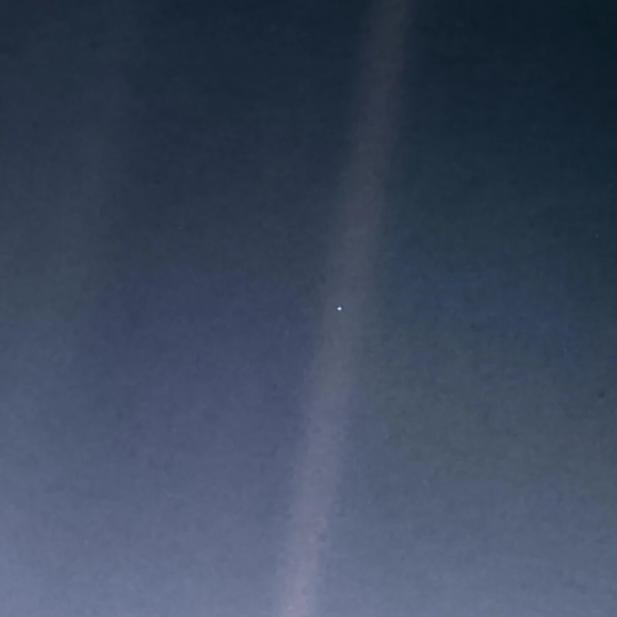 A dark blue-grey field crossed by a pale diagonal band of scattered sunlight, with Earth a single tiny bright point inside it, just right of centre.